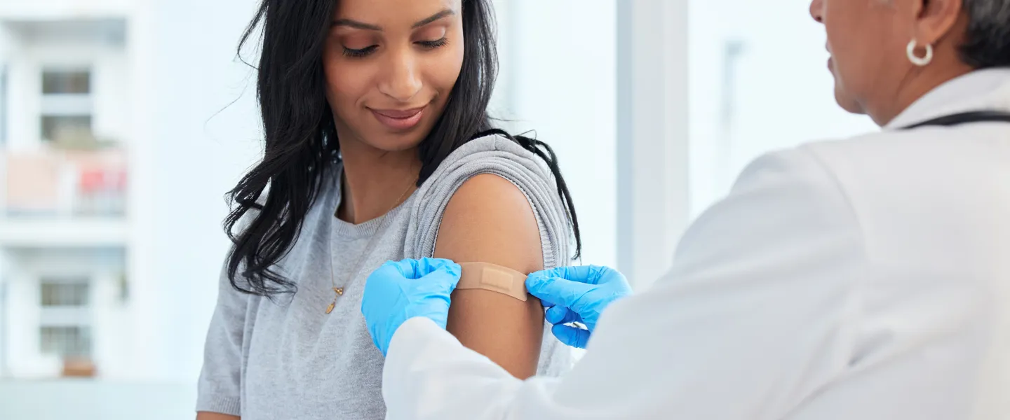 Frau bekommt von einer Ärztin ein Pflaster nach einer Impfung.
