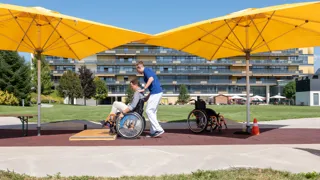 Ein Patient führt mit einem Therapeuten ein Rollstuhltraining in den Parkanlagen des RZ Häring durch.