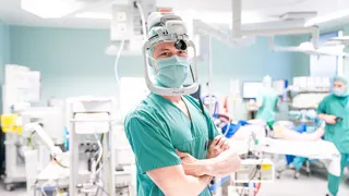 Ein Chirurg mit Mundschutz und OP-Kleidung in einem Behandlungsraum