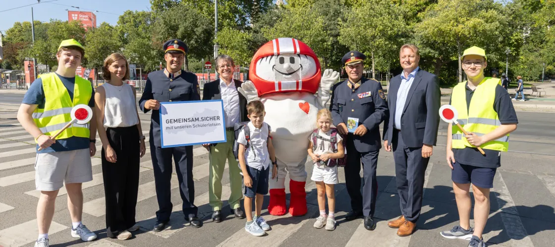 001 20250820 KFV APA Fotoservice Juhasz Erwachsene und Kinder stehen mit dem KFV-Maskottchen Helmi am Zebrastreifen