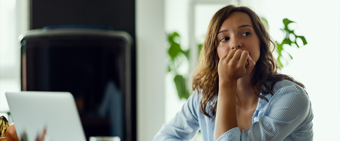 Eine nachdenklich schauende junge Frau sitzt an einem Schreibtisch und stützt ihr Kinn auf die aufgestellte Hand