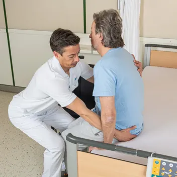 M105 Vom Querbett Sitz In Den Rollstuhl Pflegefachkraft hilft Patient vom Querbett-Sitz in den Rollstuhl