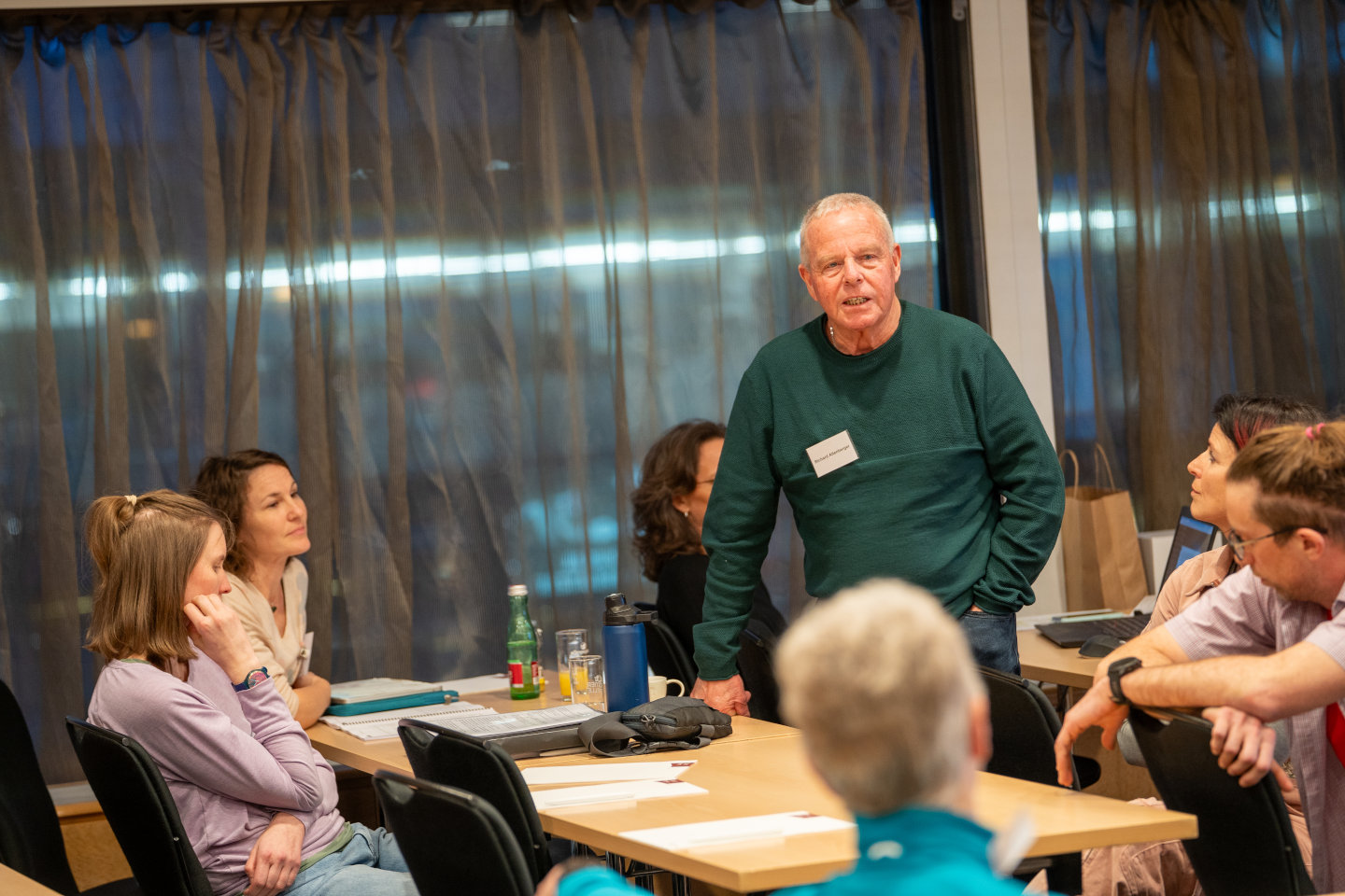 Ein Teilnehmender steht während seines Diskussionsbeitrags im Seminarraum, neben ihm sind weitere Teilnehmende im Bild
