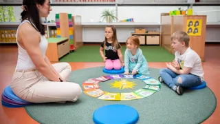 Pädagogin und drei Kindergartenkinder sitzen auf Sitzkissen im Sitzkreis