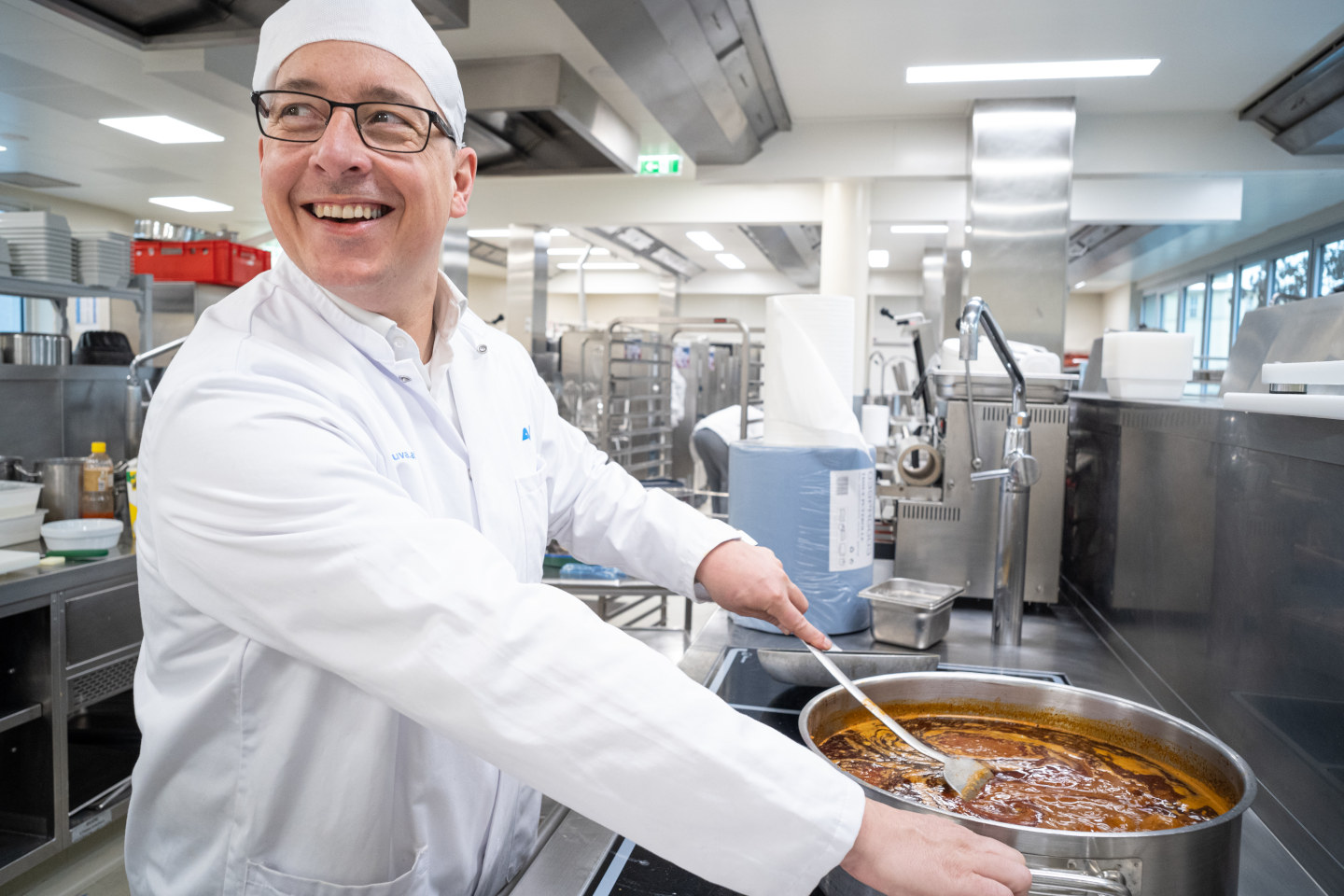 Küchenchef Stefan Lorenz rührt in der Küche des Traumazentrums Wien Meidling mit einem Kochlöffel in einem großen Topf.