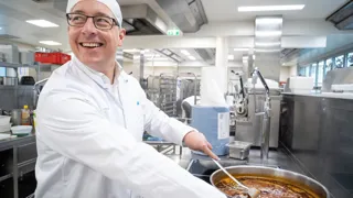 Küchenchef Stefan Lorenz rührt in der Küche des Traumazentrums Wien Meidling mit einem Kochlöffel in einem großen Topf.