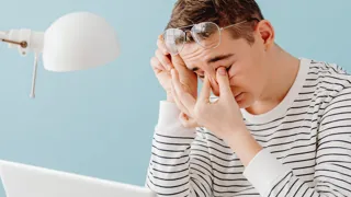 Ein Mann fasst sich bei der Büroarbeit mit den Finger an seine ermüdeten Augen Ein Mann fasst sich bei der Büroarbeit mit den Finger an seine ermüdeten Augen