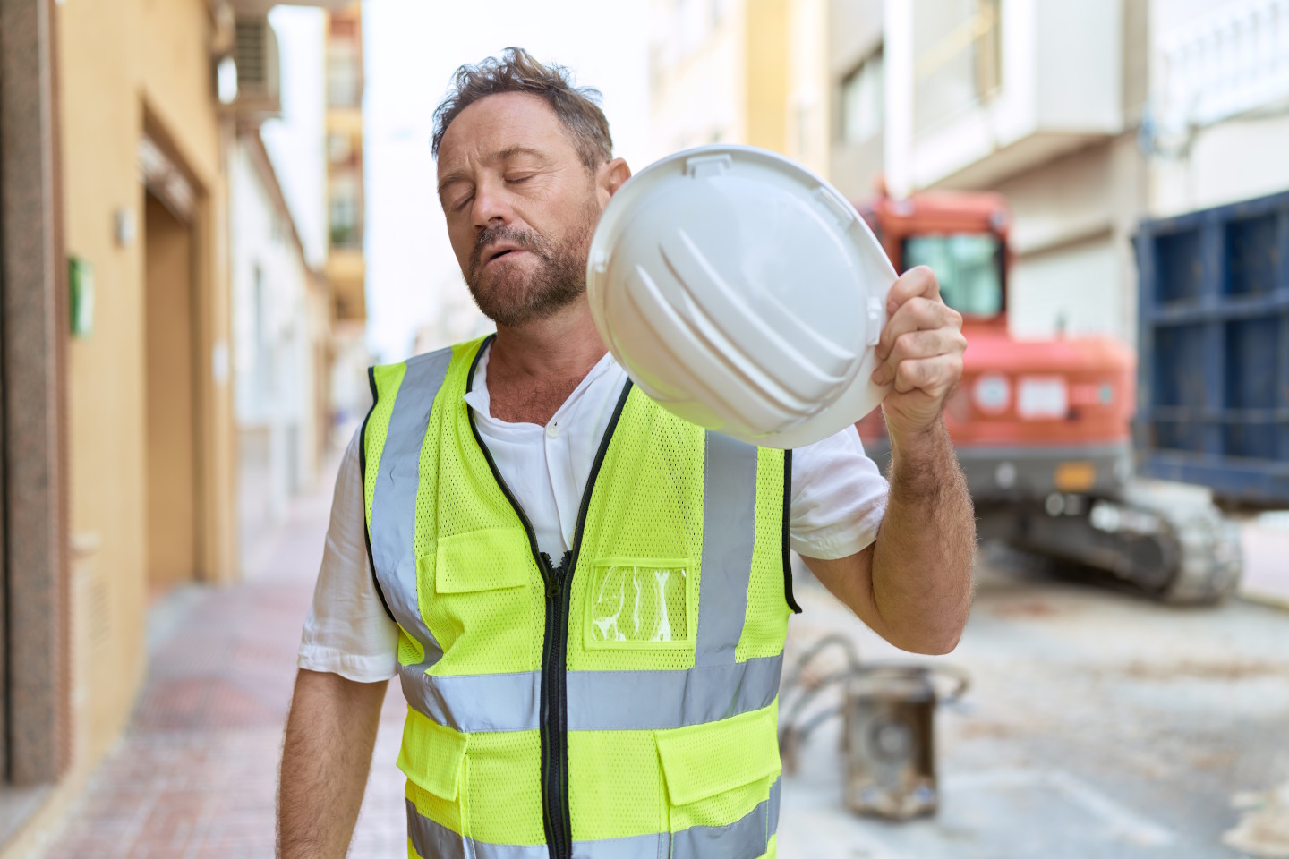 Ein Bauarbeiter hält einen Bauhelm in der Hand und fächelt sich Luft zu