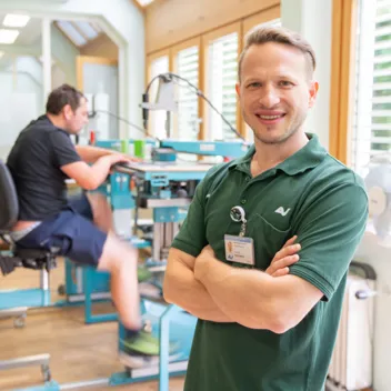 Ergotherapeut steht vorne, hinten arbeitet ein Patient an einer Werkbank Ergotherapeut steht vorne, hinten arbeitet ein Patient an einer Werkbank