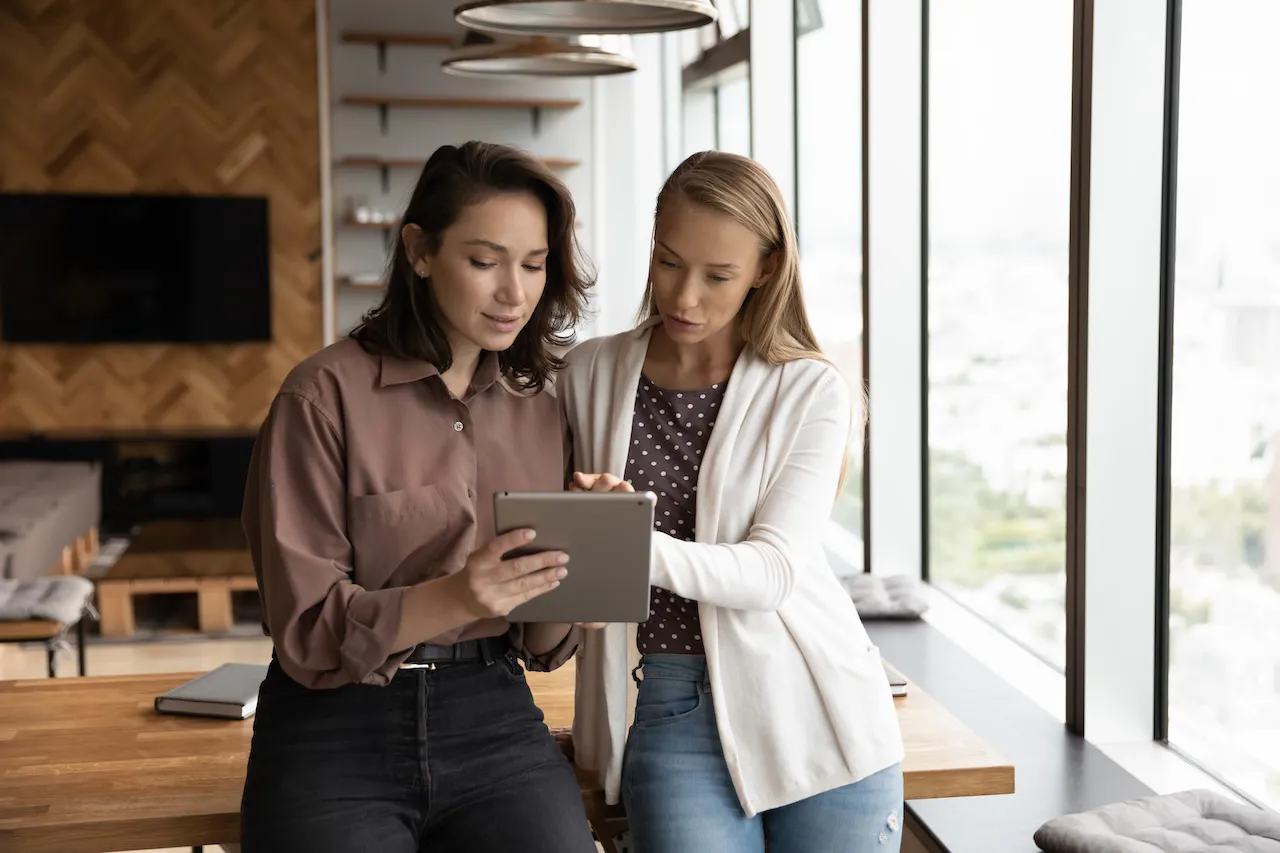 4.1.4.13_Evaluierung Belastungen_AdobeStock_450038518.jpeg Zwei Frauen besprechen am Tablet Evaluierungsergebnisse.