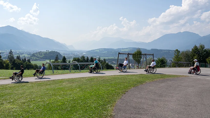Sechs Personen beim Üben der Kipptechnik im Rollstuhl - zum Bewältigen von Hindernissen im Außenbereich Sechs Personen beim Üben der Kipptechnik im Rollstuhl - zum Bewältigen von Hindernissen im Außenbereich