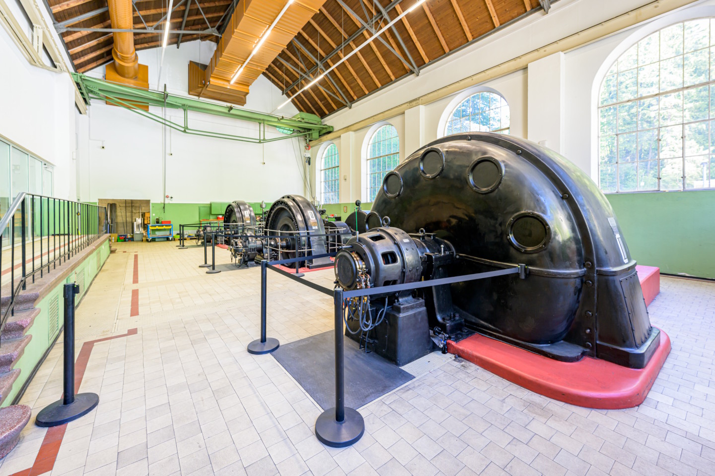 Blick in eine Turbinenhalle eines Kraftwerks. Man sieht drei große, schwarze Generatoren.