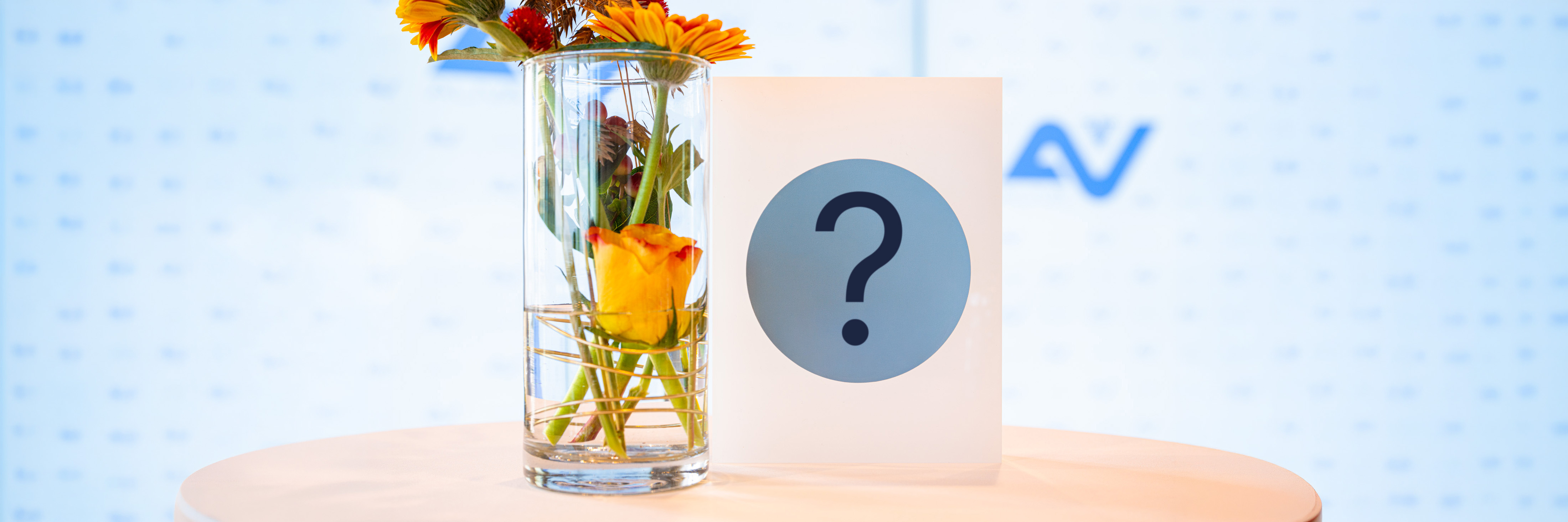 Blumenvase und weiße Trophäe mit Fragezeichen-Sticker vor einer AUVA-Logowand