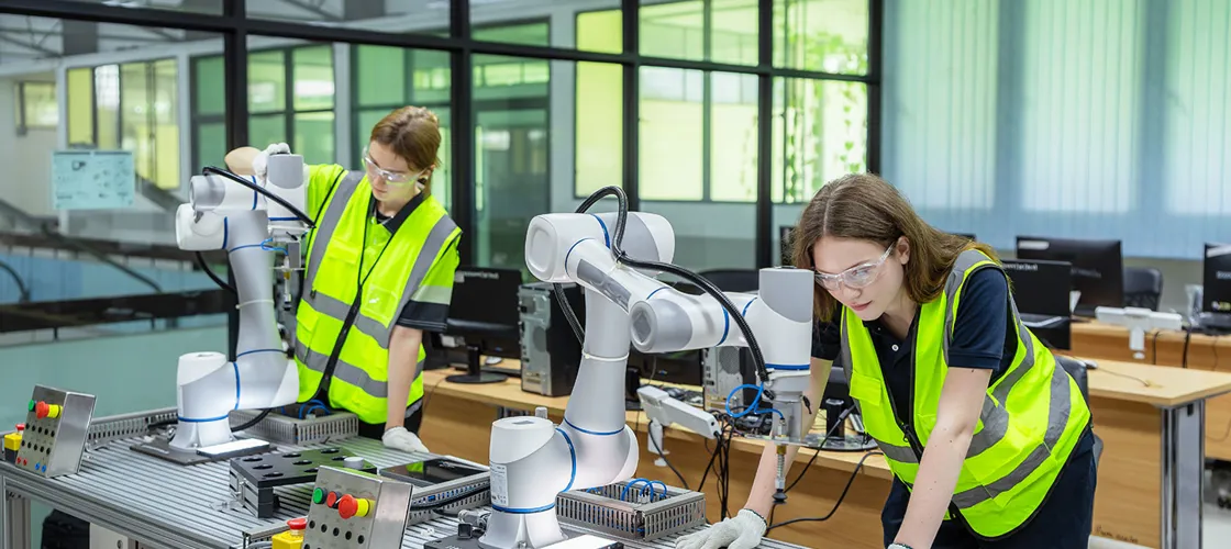 Adobestock 1599958487 Web Credit Adobestock Vstudio Zwei Frauen in Warnwesten hantieren mit Robotern, die auf einem Tisch stehen.