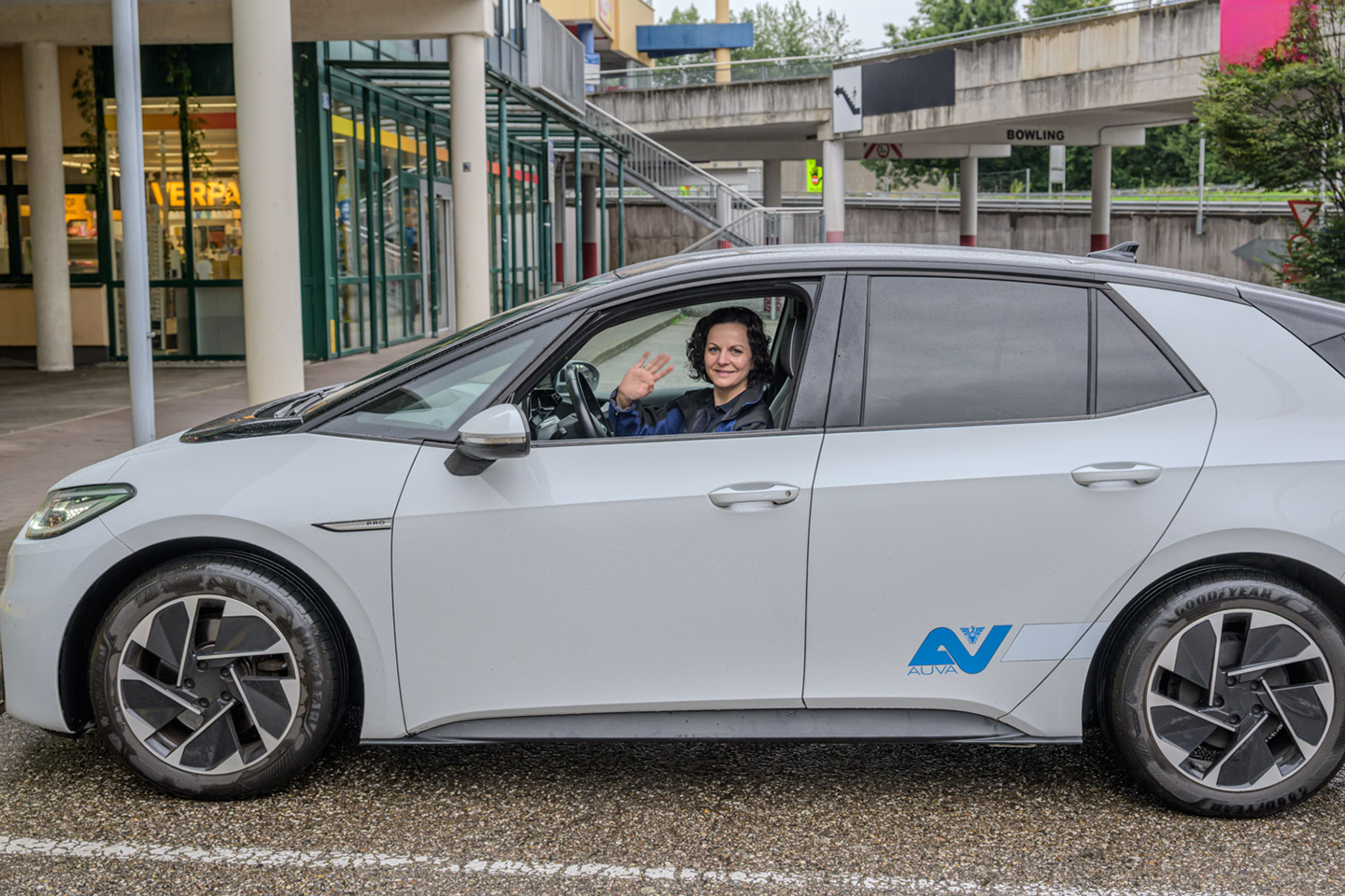Eine Frau sitzt am Fahrersitz eines PKW und winkt aus dem Fenster