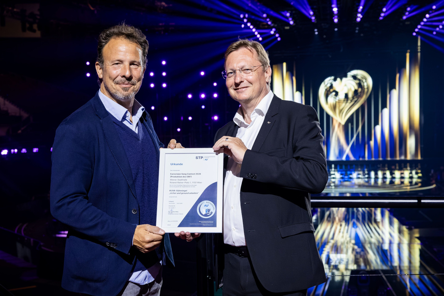 Michael Krön (Executive Producer des Eurovision Song Contest) und Roland Pichler (Stv. Generaldirektor der AUVA) präsentieren in der Stadthalle Wien die Gütesiegel-Urkunde