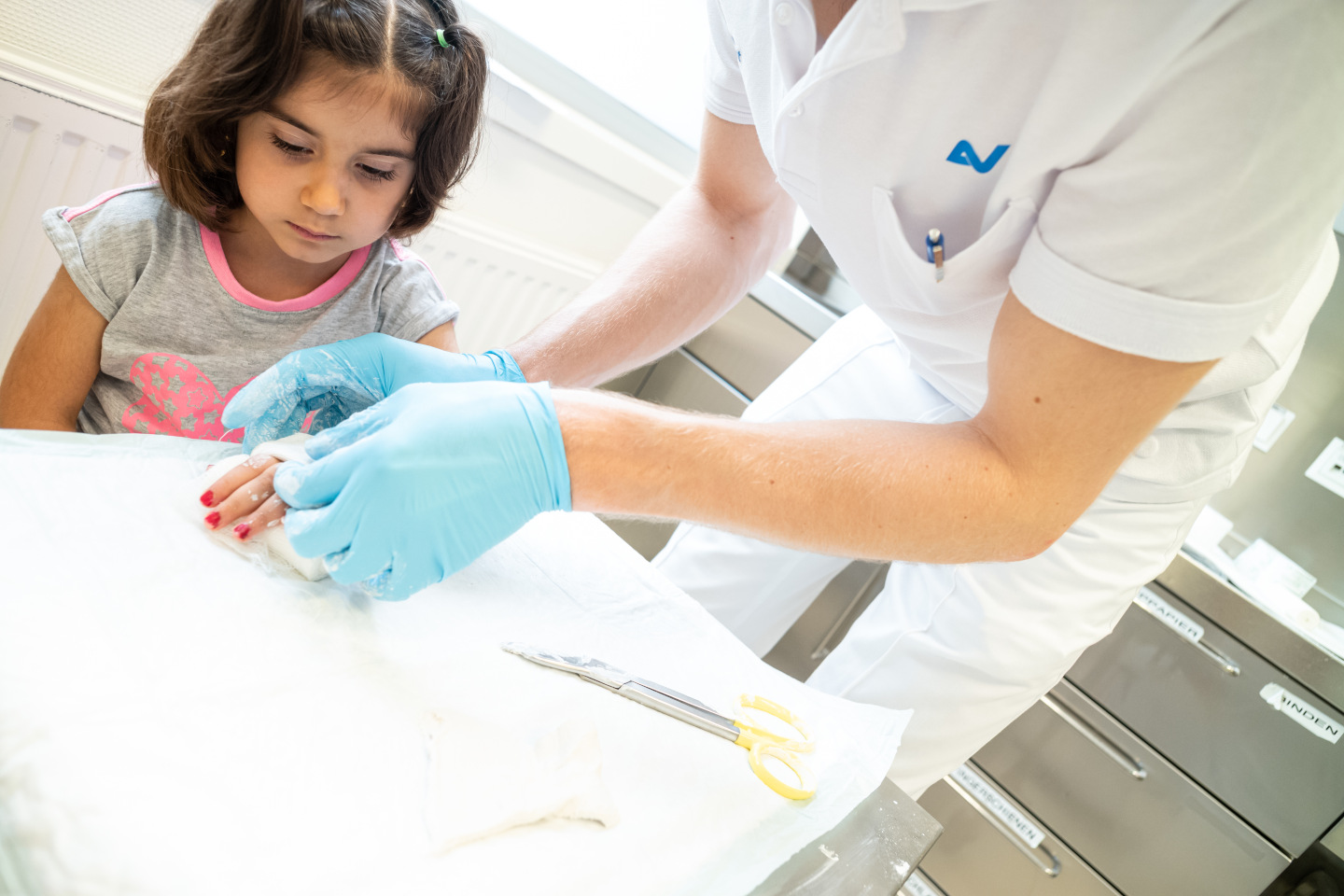 Einem Mädchen wird von einem Arzt in einem Behandlungszimmer seine verletzte Hand eingegipst.