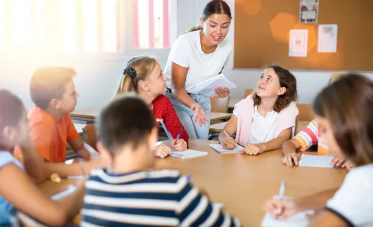 Gruppe Schüler:innen an einem runden Tisch Eine Gruppe Schüler:innen an einem runden Tisch erhält von der Lehrperson gerade eine Erklärung