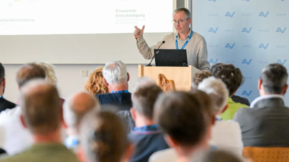 Ein Mann steht hinter einem Rednerpult und hält einen Vortrag vor einem Publikum