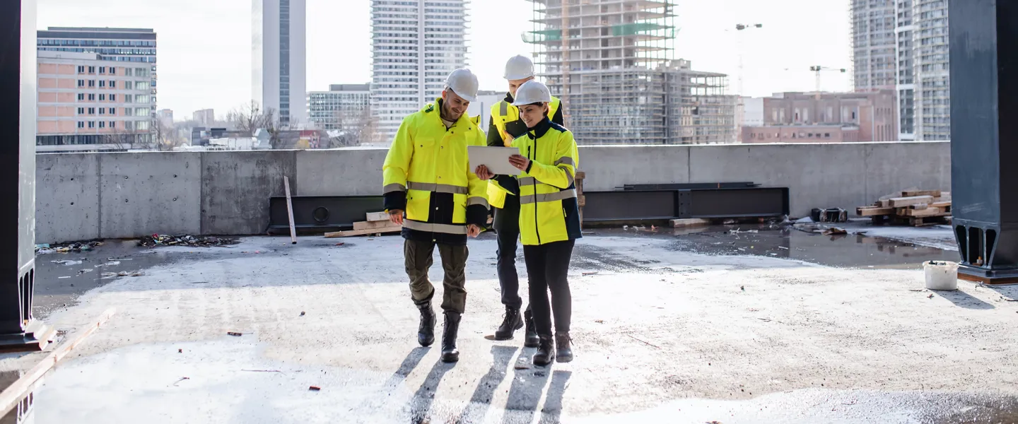 Bau Messung und Beratung Drei Personen auf einer Baustelle. Die Ingenieurin nutzen ein Tablet zur Überprüfung.