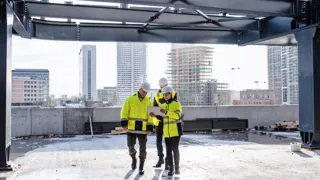Bau Messung und Beratung Drei Personen auf einer Baustelle. Die Ingenieurin nutzen ein Tablet zur Überprüfung.