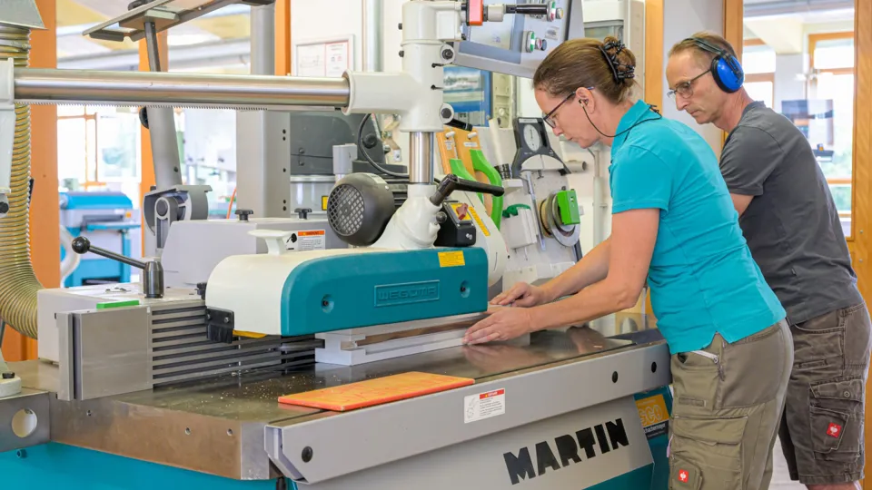 drei Erwachsene beim Arbeiten an einer Holzkreissäge