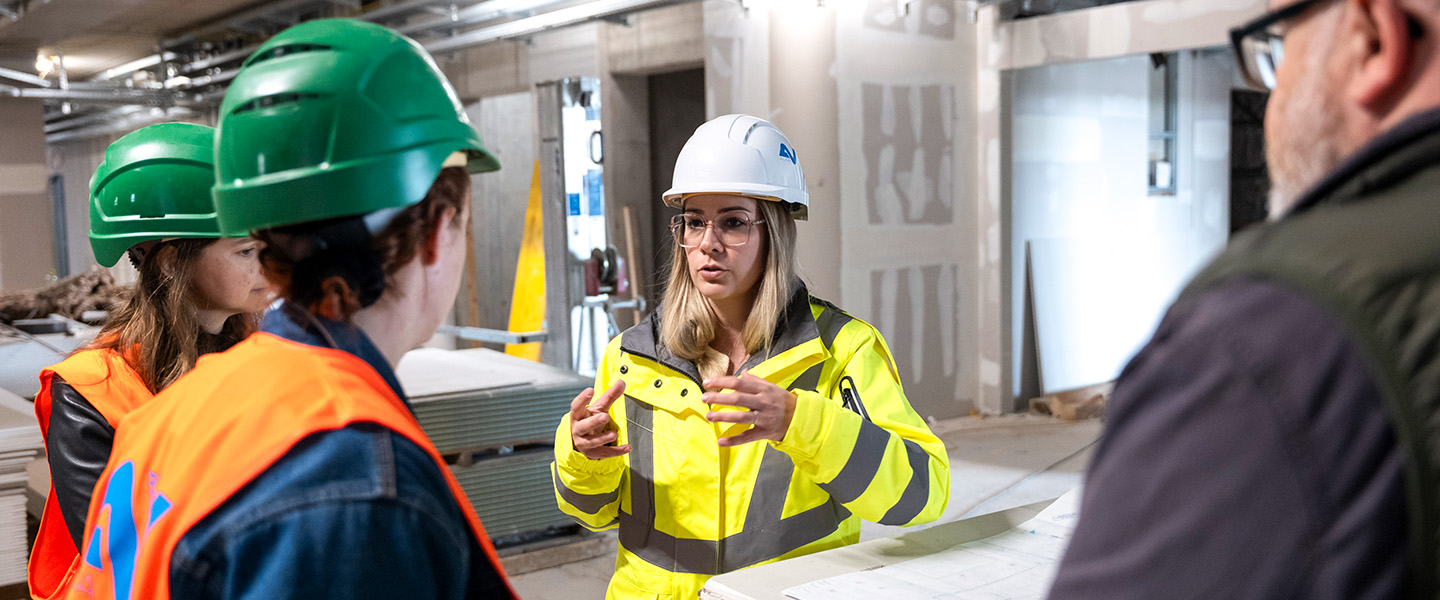 AUVA-Mitarbeiterin Teresa Skalsky auf der Baustelle des Rehabilitationszentrums Wien im Gespräch mit Mitarbeitenden aus dem Baubereich