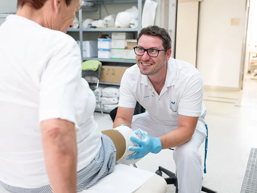 Orthopädietechniker modelliert Gips an den Amputationsstumpf einer Patientin zur Prothesenherstellung Orthopädietechniker modelliert Gips an den Amputationsstumpf einer Patientin zur Prothesenherstellung