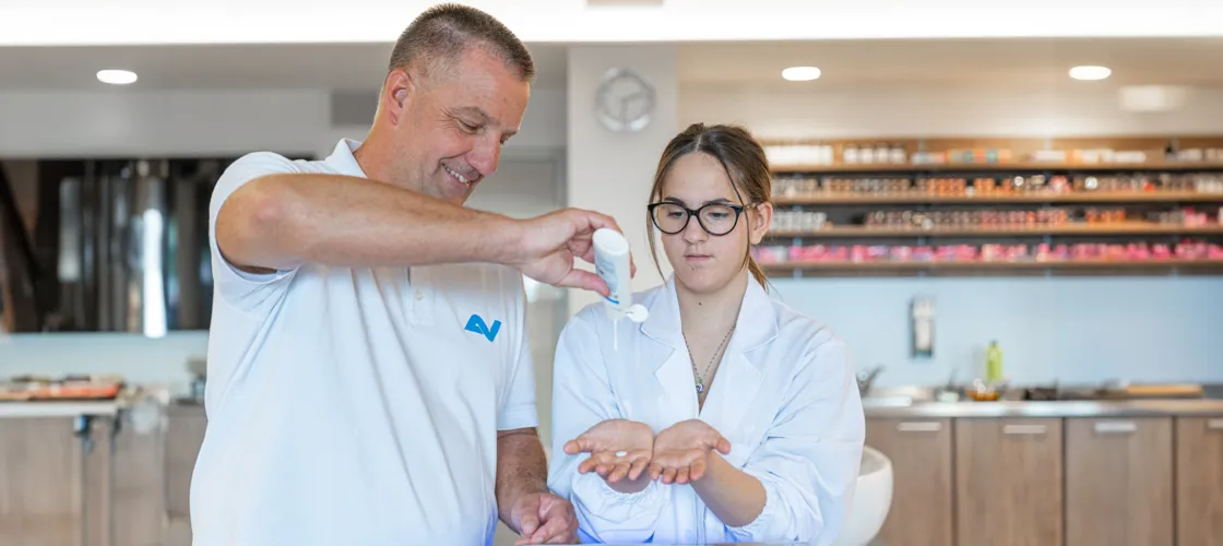 Arbeitsmediziner erklärt weiblichem Friseur-Lehrling das richtige Eincremen der Hände. Arbeitsmediziner
