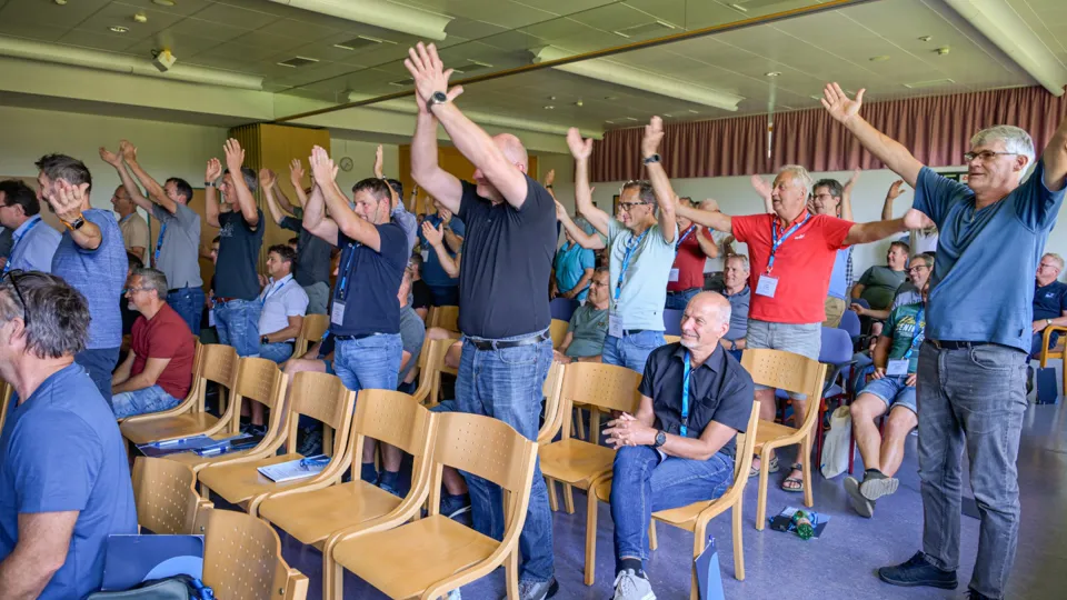 Mehrere Menschen in einem Vortragssaal stehen und halten die Arme in die Luft