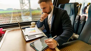Mann arbeitet im Zug auf Laptop und Tablet.