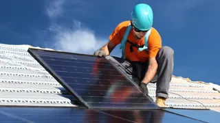 Ein Arbeiter montiert ein Photovoltaik-Paneel auf einem Dach 