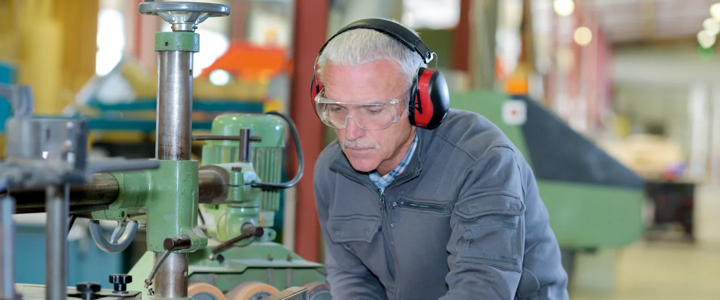 213611461 Handwerker In Tischlerei Mit Gehorschutz 1440 ZUSCHNITT Credit Auremar Adobestock Ein älterer Mann mit Kapselgehörschutz arbeitet an einer Maschine