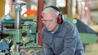 213611461 Handwerker In Tischlerei Mit Gehorschutz 1440 ZUSCHNITT Credit Auremar Adobestock Ein älterer Mann mit Kapselgehörschutz arbeitet an einer Maschine