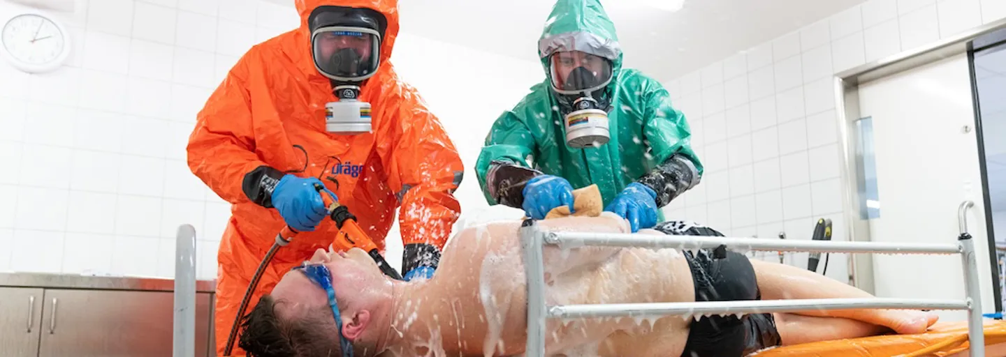 Dekontaminationsübung: Zwei Einsatzkräfte in Schutzkleidung dekontaminieren eine auf einer Trage liegende kontaminierte Person  Dekontaminationsübung: Zwei Einsatzkräfte in Schutzkleidung dekontaminieren eine auf einer Trage liegende kontaminierte Person