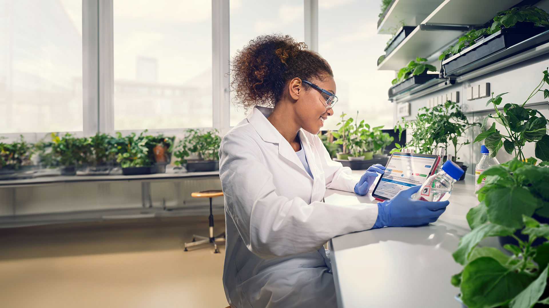 Frau im Pflanzenlabor überprüft mittels Arbeitsstoffverzeichnis am Tablet die Eigenschaften der Chemikalien, um eine fehlerhafte Anwendung zu vermeiden.