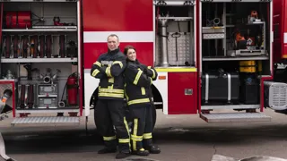 weißer Feuerwehr Schriftzug auf rotem Feuerwehrauto Feuerwehrmann und Feuerwehrfrau stehen nebeneinander vor einem Feuerwehrfahrzeug