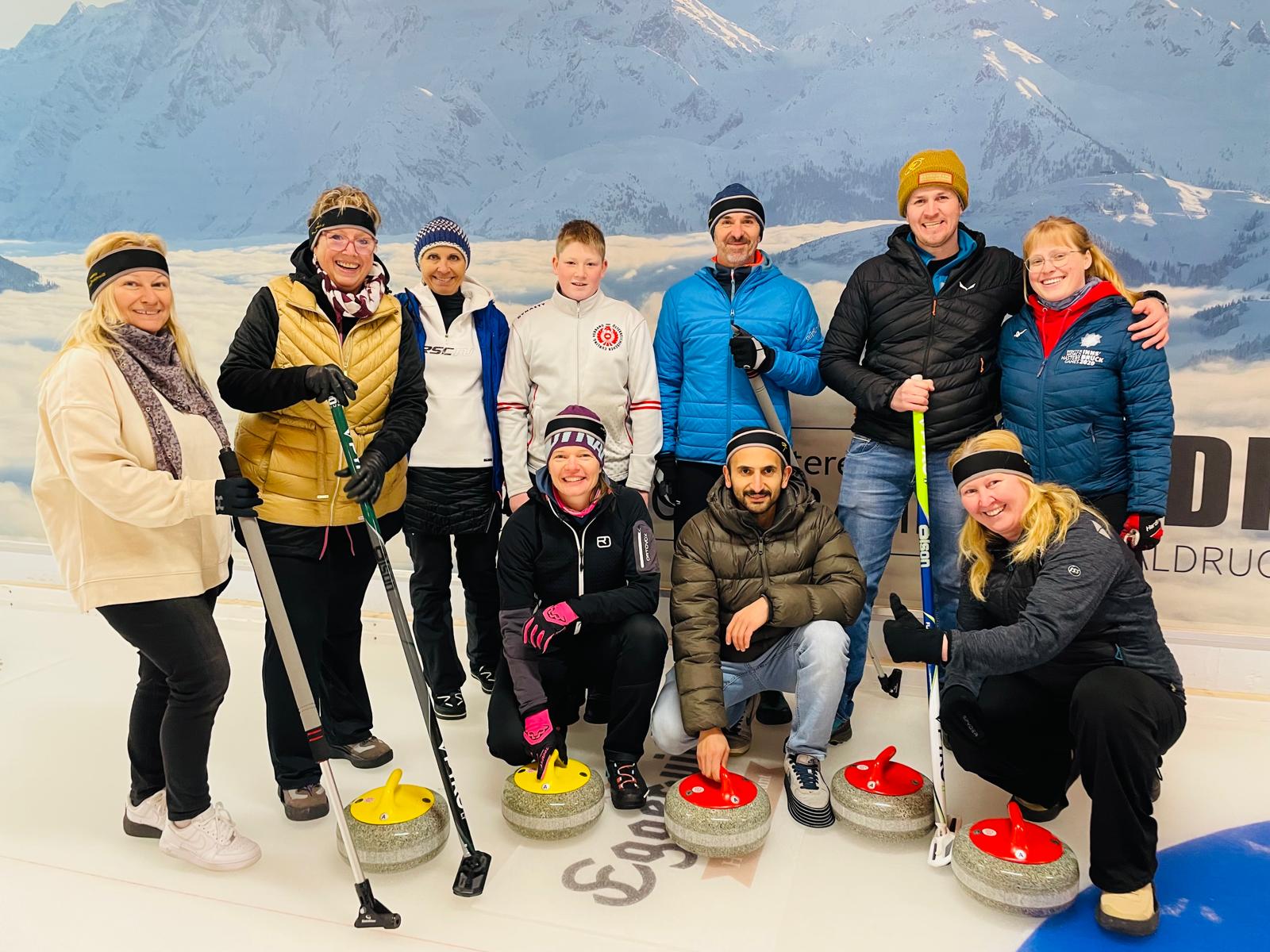 Gruppenbild der Teilnehmenden am Eis mit Curling-Ausrüstung