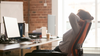 Eine Frau lehnt sich in ihrem Schreibtischstuhl nach hinten, um sich bei der Büroarbeit kurz zu entspannen
