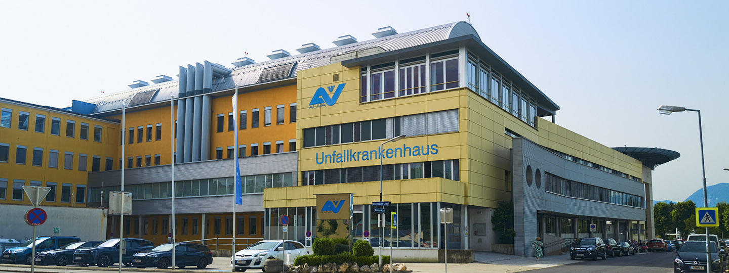 Außenansicht UKH Klagenfurt am Wörthersee, umgeben von geparkten Autos und Straße.