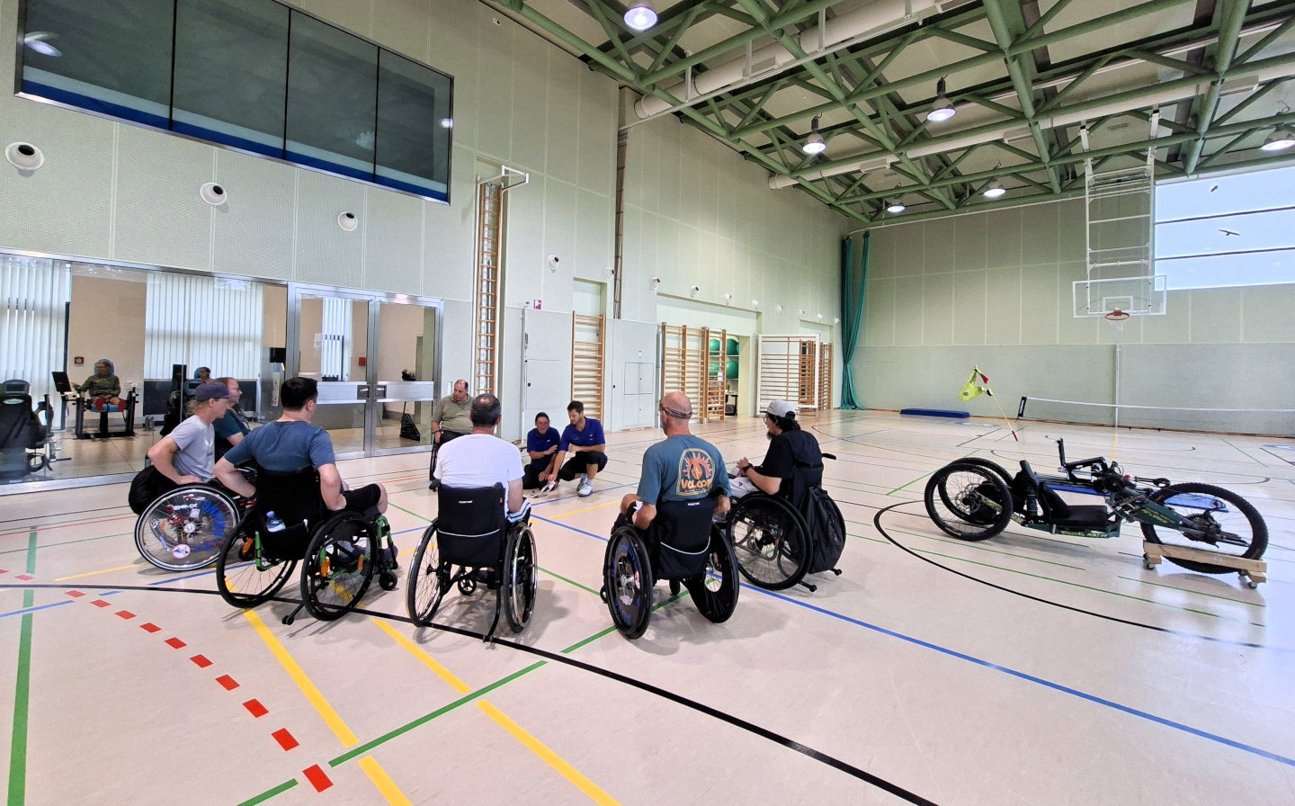Patientinnen und Patienten im Rollstuhl verfolgen im Turnsaal des Parasportzentrums Häring die Präsentation eines umgebauten E-Bikes für Menschen mit Querschnittlähmung.