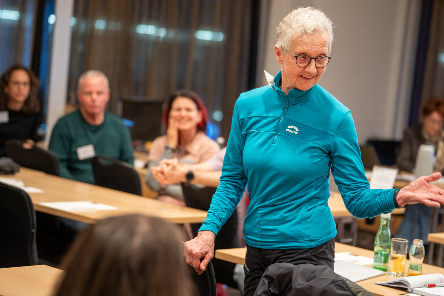 Teilnehmende steht während ihres Diskussionsbeitrags im Seminarraum, neben ihr sind weitere Teilnehmende im Bild