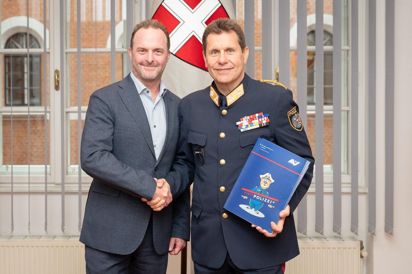 AUVA-Generaldirektor Mag. Alexander Bernart und Bundespolizeidirektor Michael Takács schauen in die Kamera und geben sich die Hand