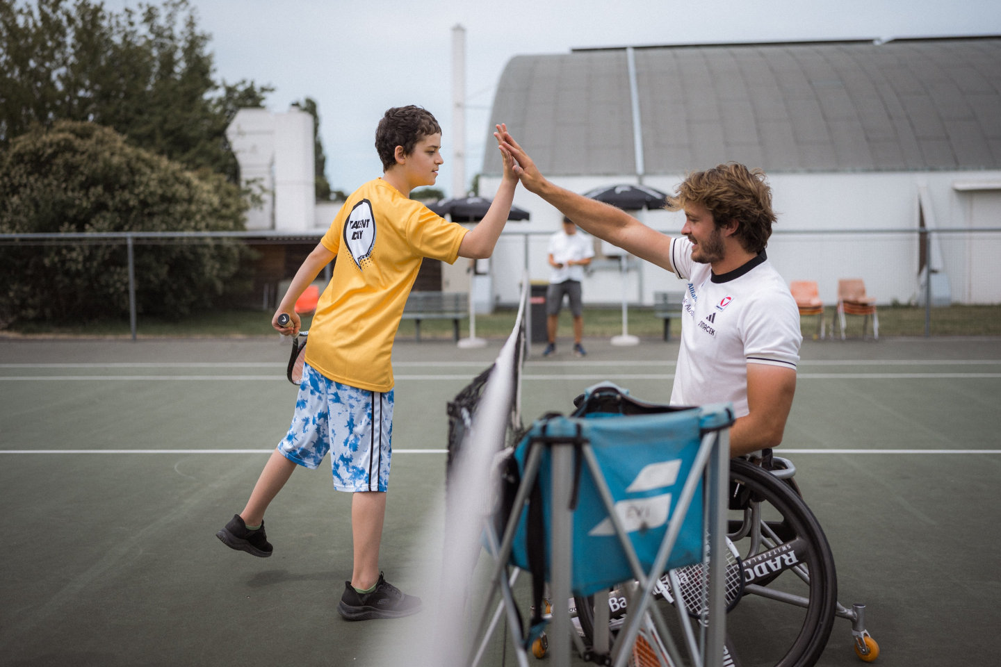 Rohlstuhltennisspieler Nico Langmann klatscht auf dem Tennisfeld mit einem Jungen ab