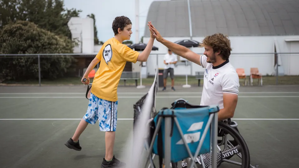 Rohlstuhltennisspieler Nico Langmann klatscht auf dem Tennisfeld mit einem Jungen ab