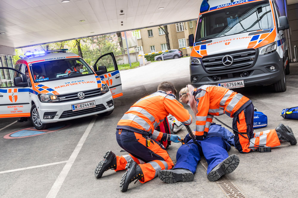 Sanitäter:in bei Einsatz-Übung mit Notarzt-Einsatz-Fahrzeug (NEF) im Hintergrund