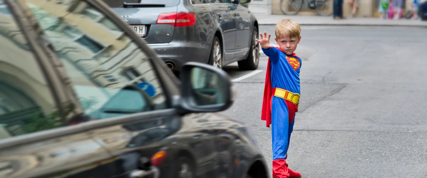 Ein Junge im Supermannkostüm steht vor einem Auto. Aktionen