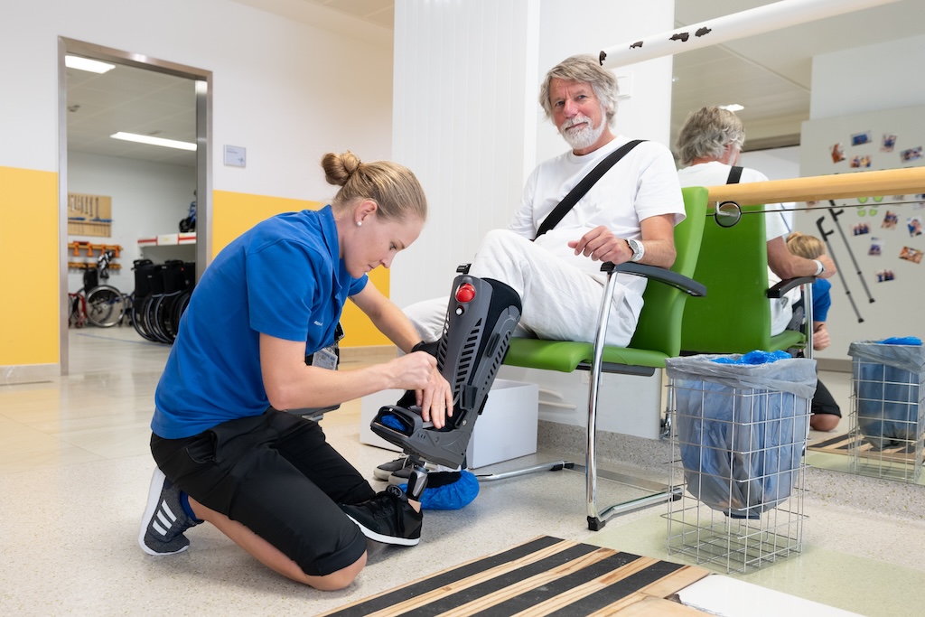 Eine Mitarbeiterin des Rehazentrums legt einem Patienten eine Beinprothese an.