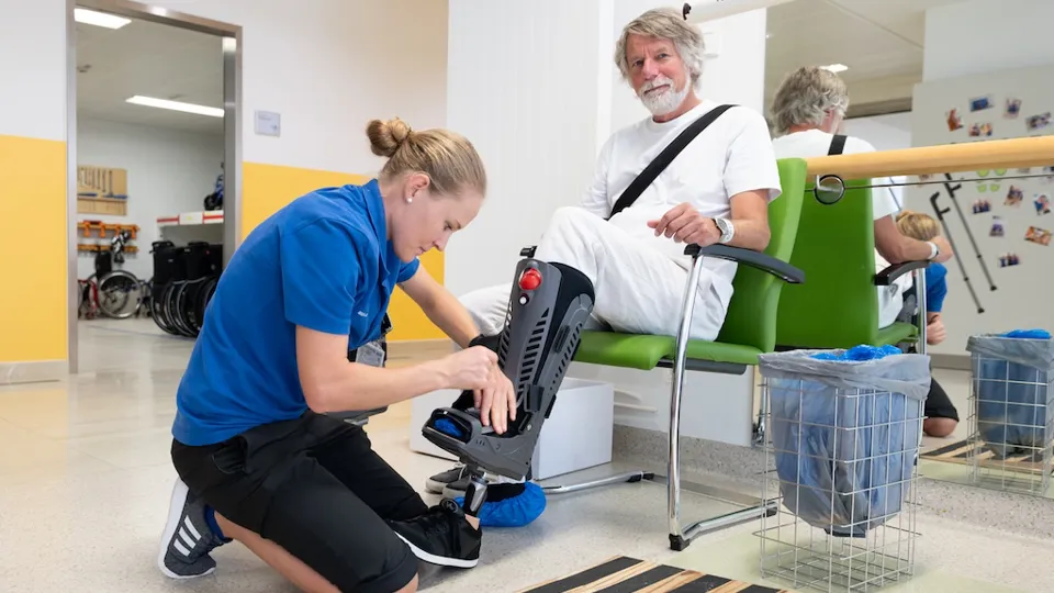 Eine Mitarbeiterin des Rehazentrums legt einem Patienten eine Beinprothese an.