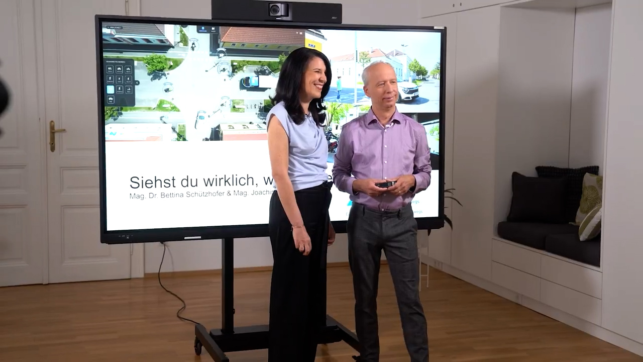 Eine Frau und ein Mann stehen vor einem großen Fernseher